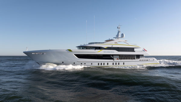 A luxury yacht cruising on open water under a clear blue sky, with waves forming around the hull.