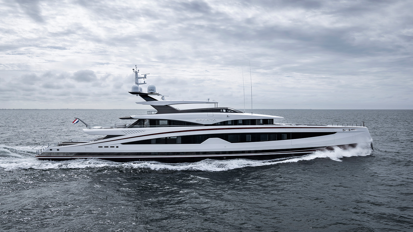 A luxury yacht named Sparta cruising on the ocean under a cloudy sky, with waves splashing around its bow.
