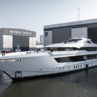 A luxury yacht being launched from the Heesen Yachts facility into the water, surrounded by buildings and vehicles.