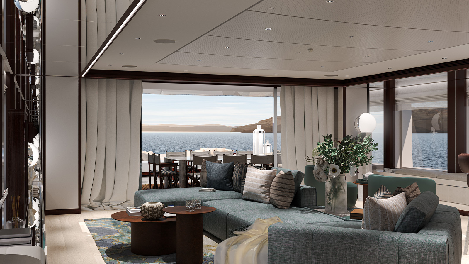 Luxurious yacht interior featuring a spacious living area with a large sectional sofa, coffee tables, and decorative cushions, overlooking a dining area through open sliding doors, with a view of the sea and distant hills.