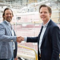 Laurens Last and Niels Vaessen, CEO of Heesen Yachts, shaking hands in a construction area with scaffolding and industrial equipment in the background.
