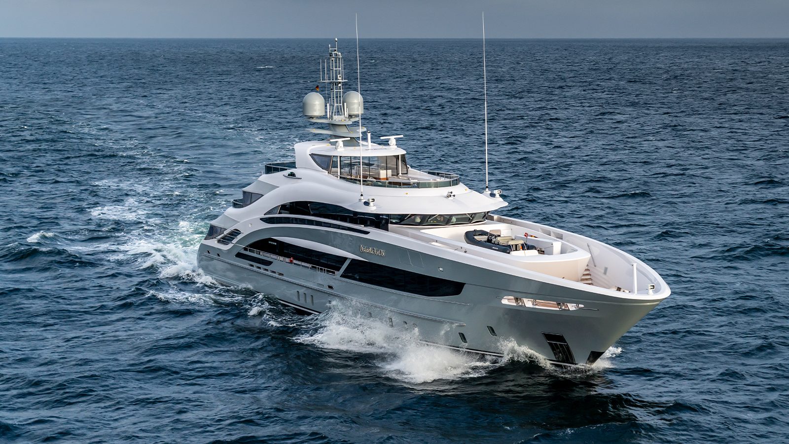 A large, sleek white yacht cruising through open water with visible waves around it under a cloudy sky.