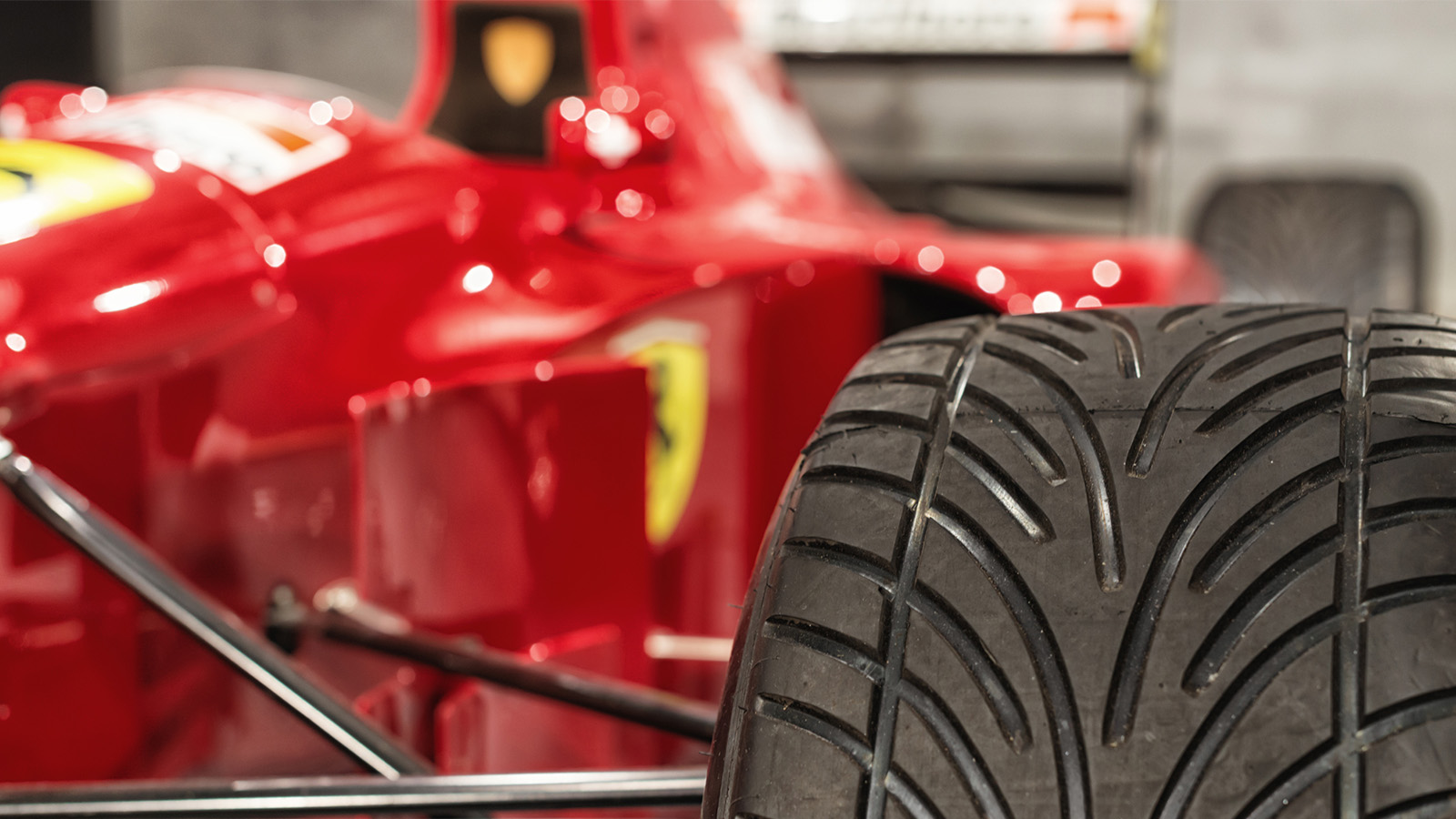 Close-up of a rear tire on a red Formula 1 race car, featuring detailed tread patterns and part of the car's body and logo visible in the background.