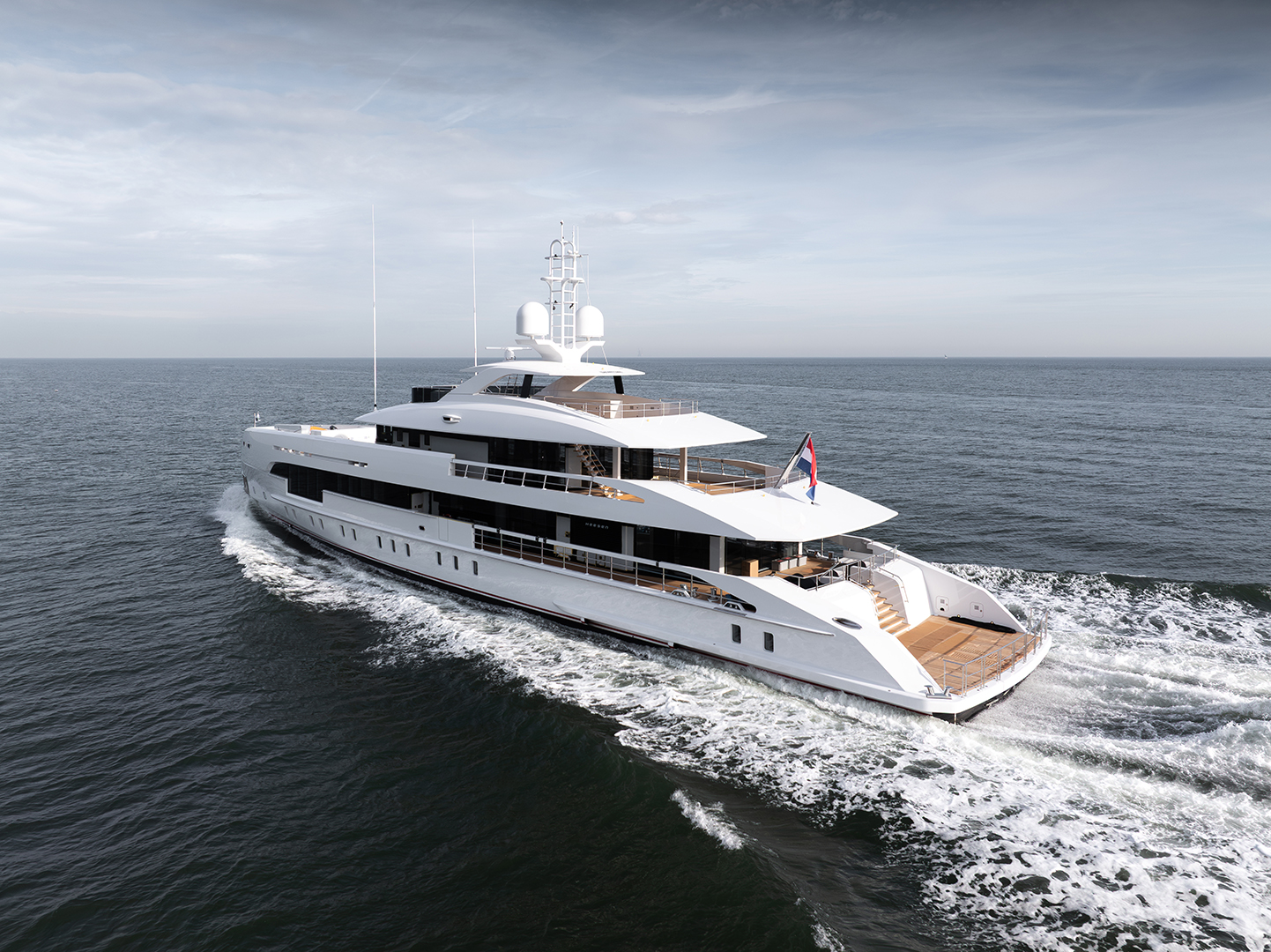 A large white yacht cruising on the ocean, displaying multiple decks and a flag at the stern.