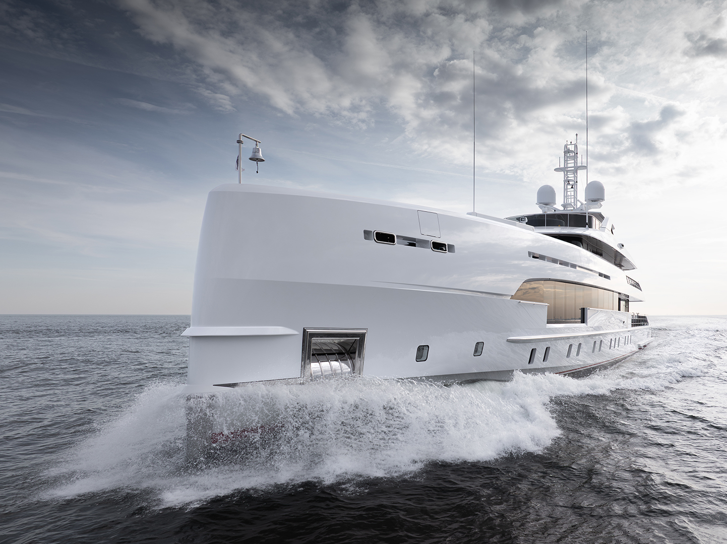 A sleek, modern yacht cutting through the ocean, with waves splashing against its white hull under a partly cloudy sky.