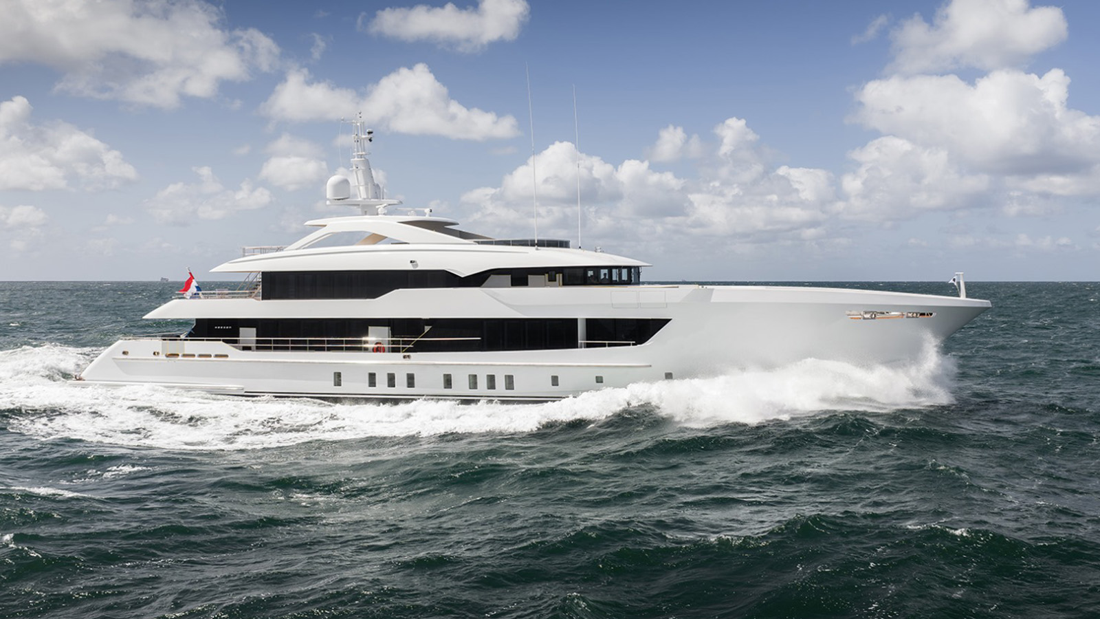 A large white luxury yacht cruising on the ocean under a partly cloudy sky.