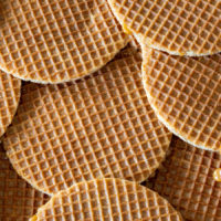 A close-up view of a pile of stroopwafels, showing their grid pattern and edges with sticky caramel filling.