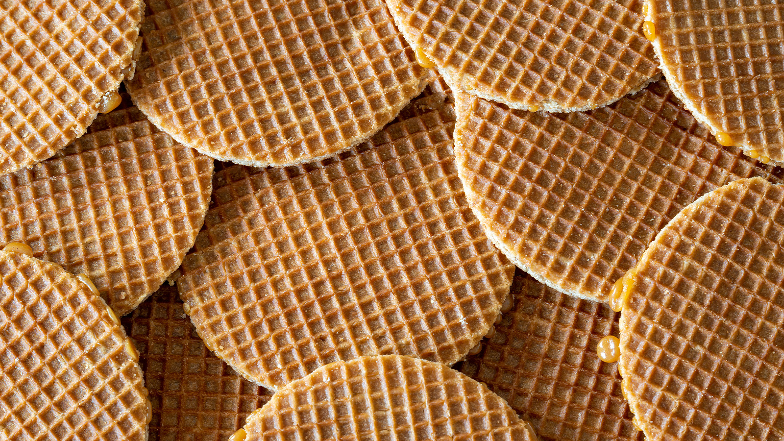 A close-up view of a pile of stroopwafels, showing their grid pattern and edges with sticky caramel filling.