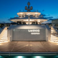 A luxury yacht named Lusine, docked at night, with its name illuminated and surrounded by softly lit staircases.
