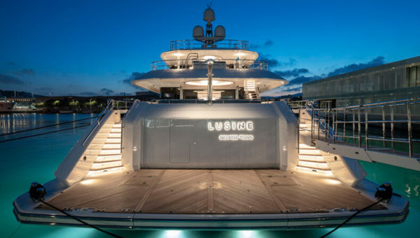 A luxury yacht named Lusine, docked at night, with its name illuminated and surrounded by softly lit staircases.