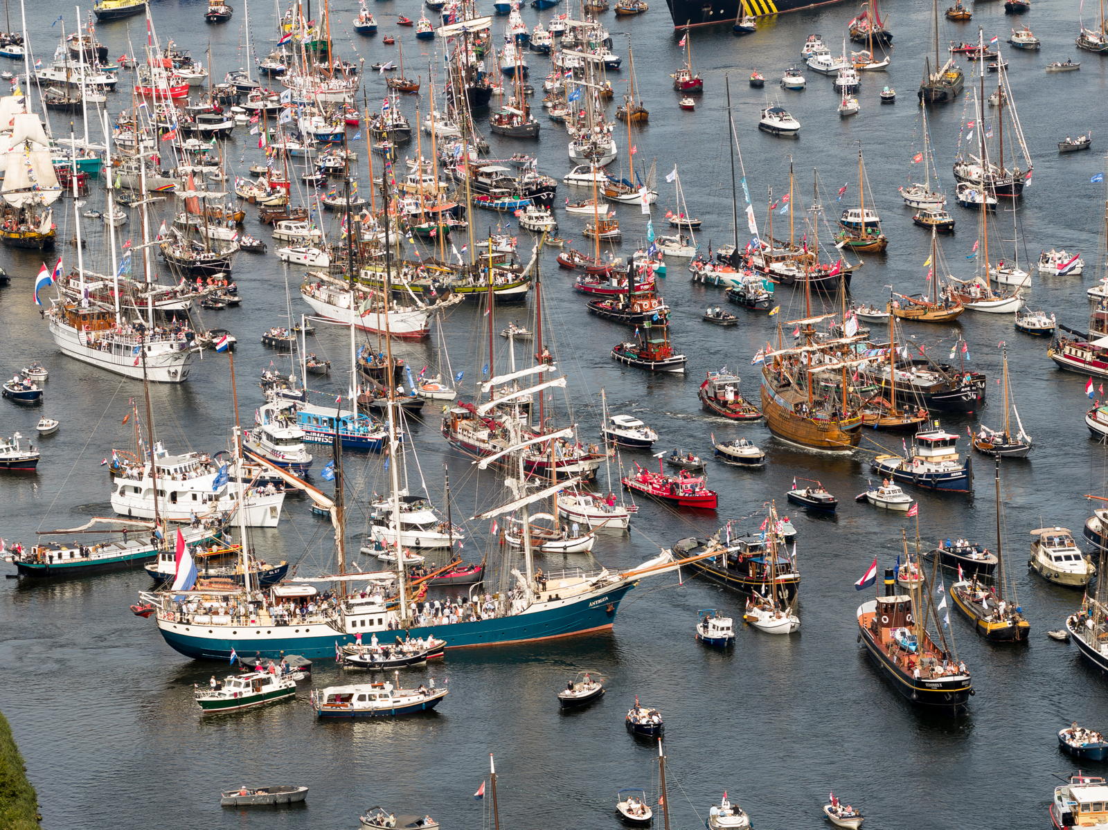 Aerial view of a crowded harbor filled with a large number of sailboats and small vessels, many displaying colorful flags and sails, suggesting a maritime event or celebration.