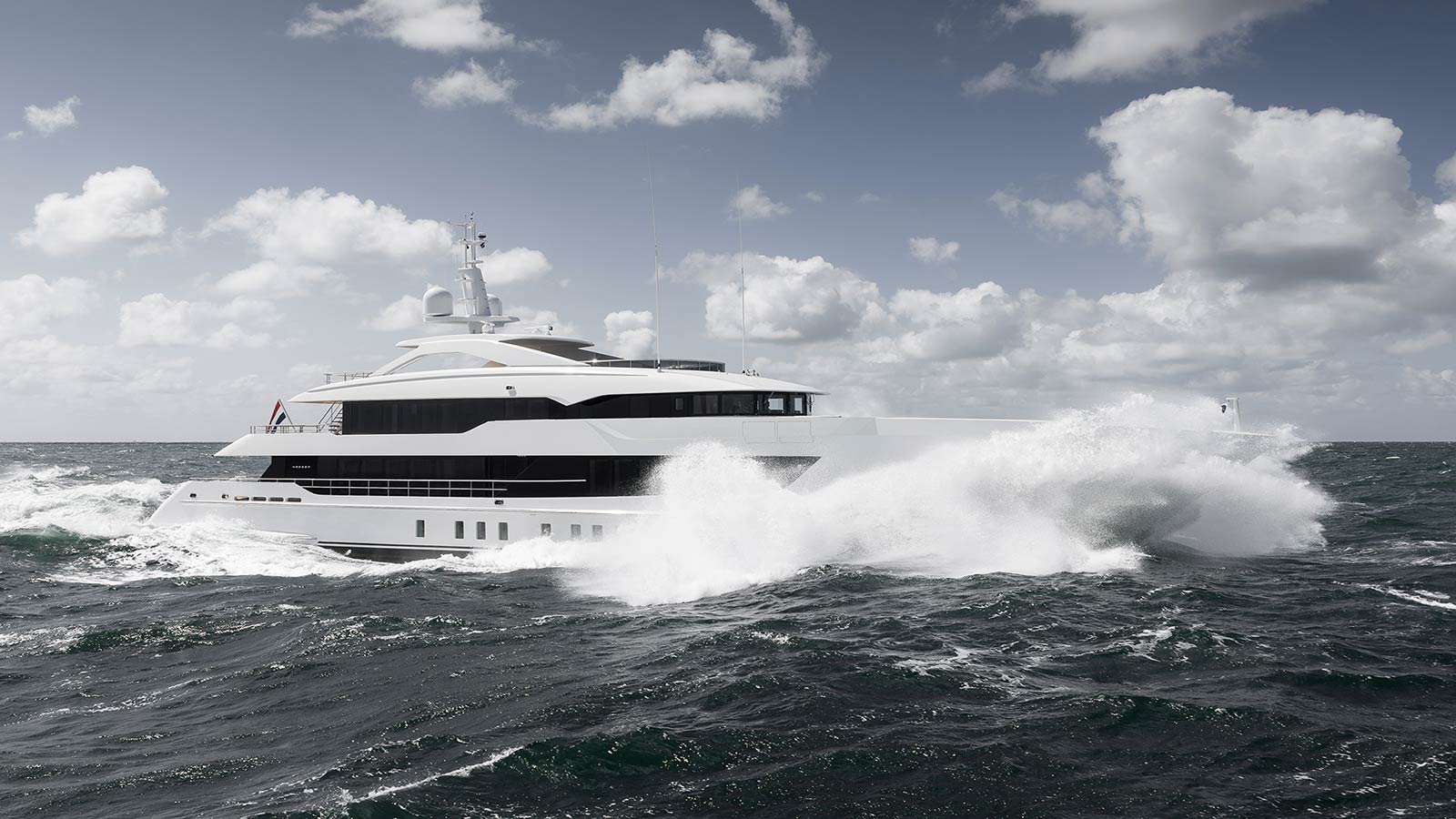 A large white yacht cruising through choppy ocean waters under a partly cloudy sky, with waves crashing against its hull.